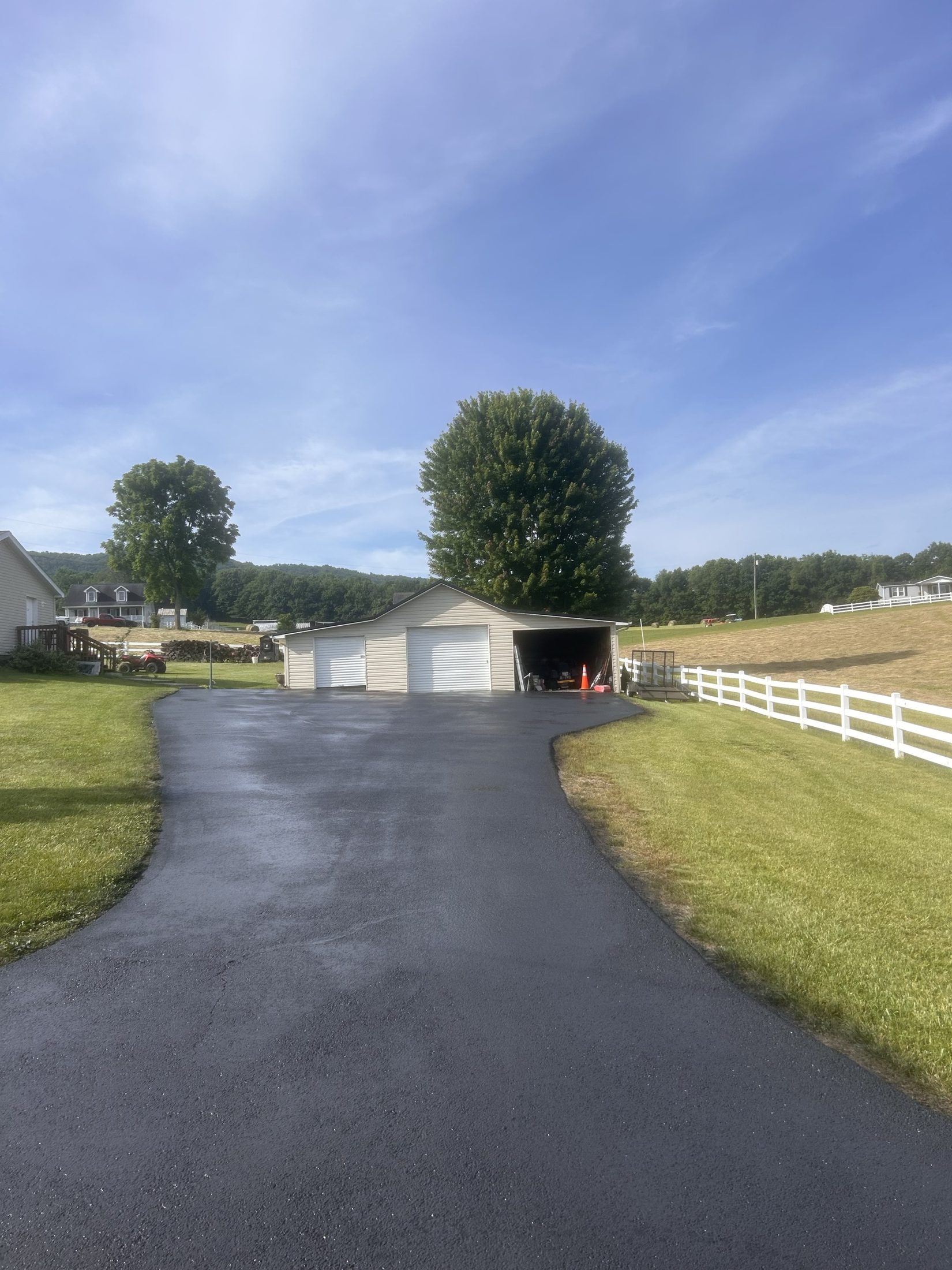 Sealcoated driveway leading to a garage with white fencing